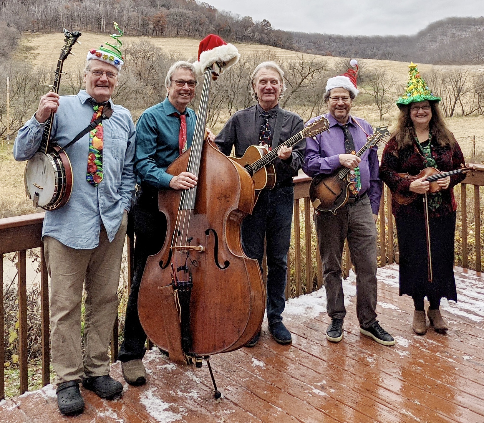 A group of five musicians stand next to each other in row. Everyone is wearing a winter holiday festive hat.